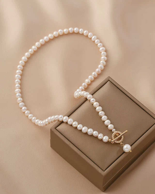 Pearl necklace with a gold clasp on a brown jewelry box against a beige background