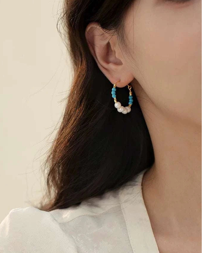 Close-up of a person wearing a black and gold hoop earring with turquoise stones.