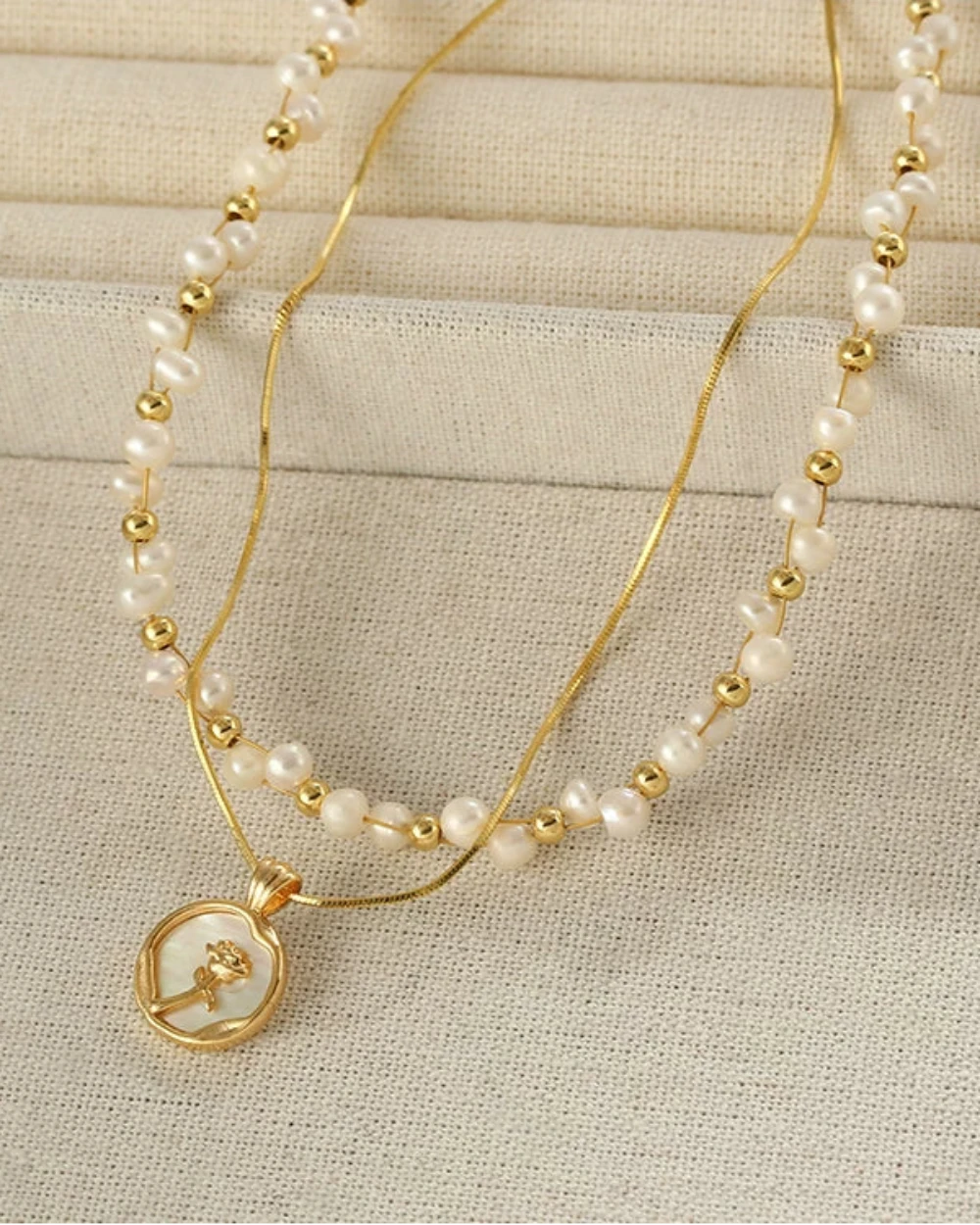 Two pearl necklaces with gold accents on a beige fabric background