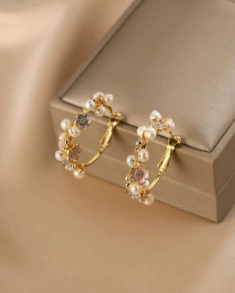 Gold hoop earrings with pearl and gemstone accents on a beige surface