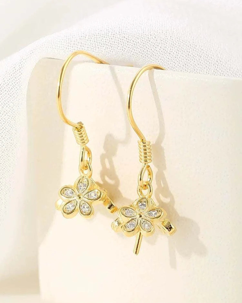 Gold four-leaf clover earrings on a soft beige background