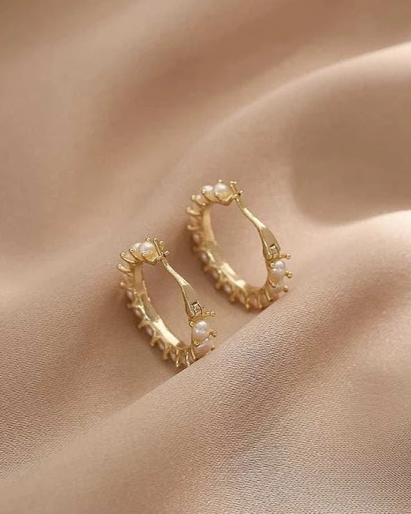 Gold hoop earrings with pearl-like stones on a beige fabric background