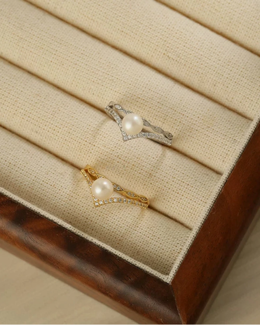 Two pearl jewelry pieces on a wooden jewelry box with beige interior