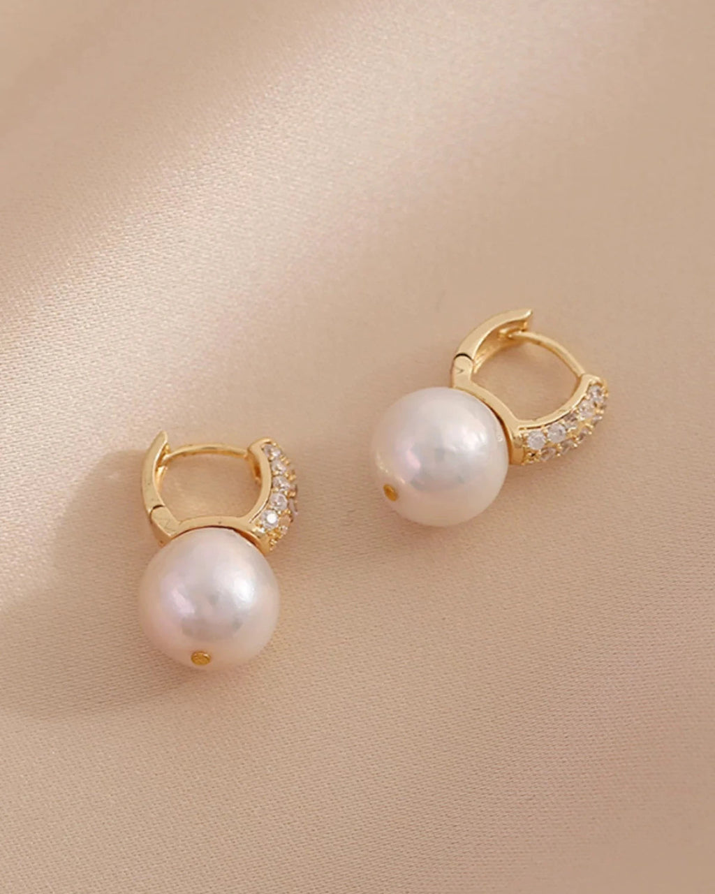 Pair of pearl earrings with gold accents on a beige background