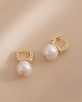 Pair of pearl earrings with gold accents on a beige background
