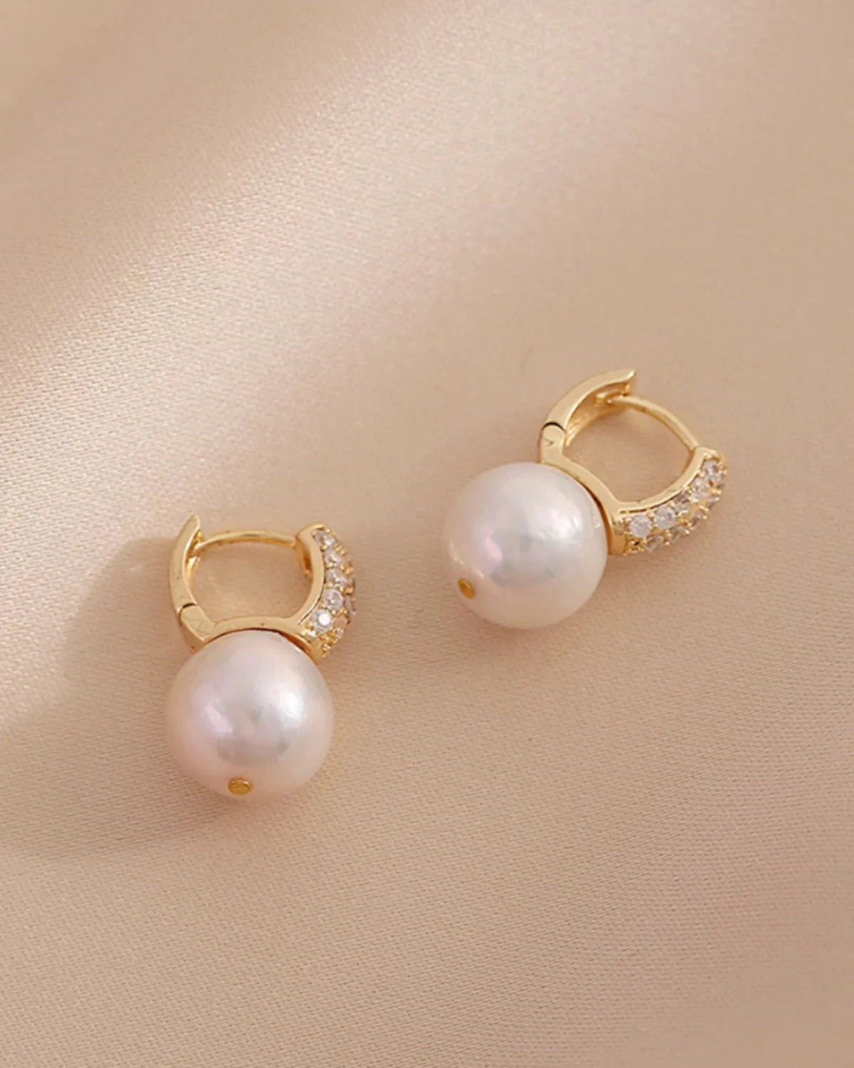 Pair of pearl earrings with gold accents on a beige background