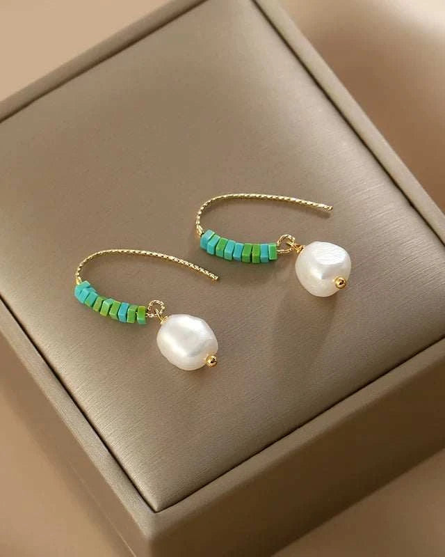 Pair of pearl and turquoise beaded earrings on a beige jewelry box