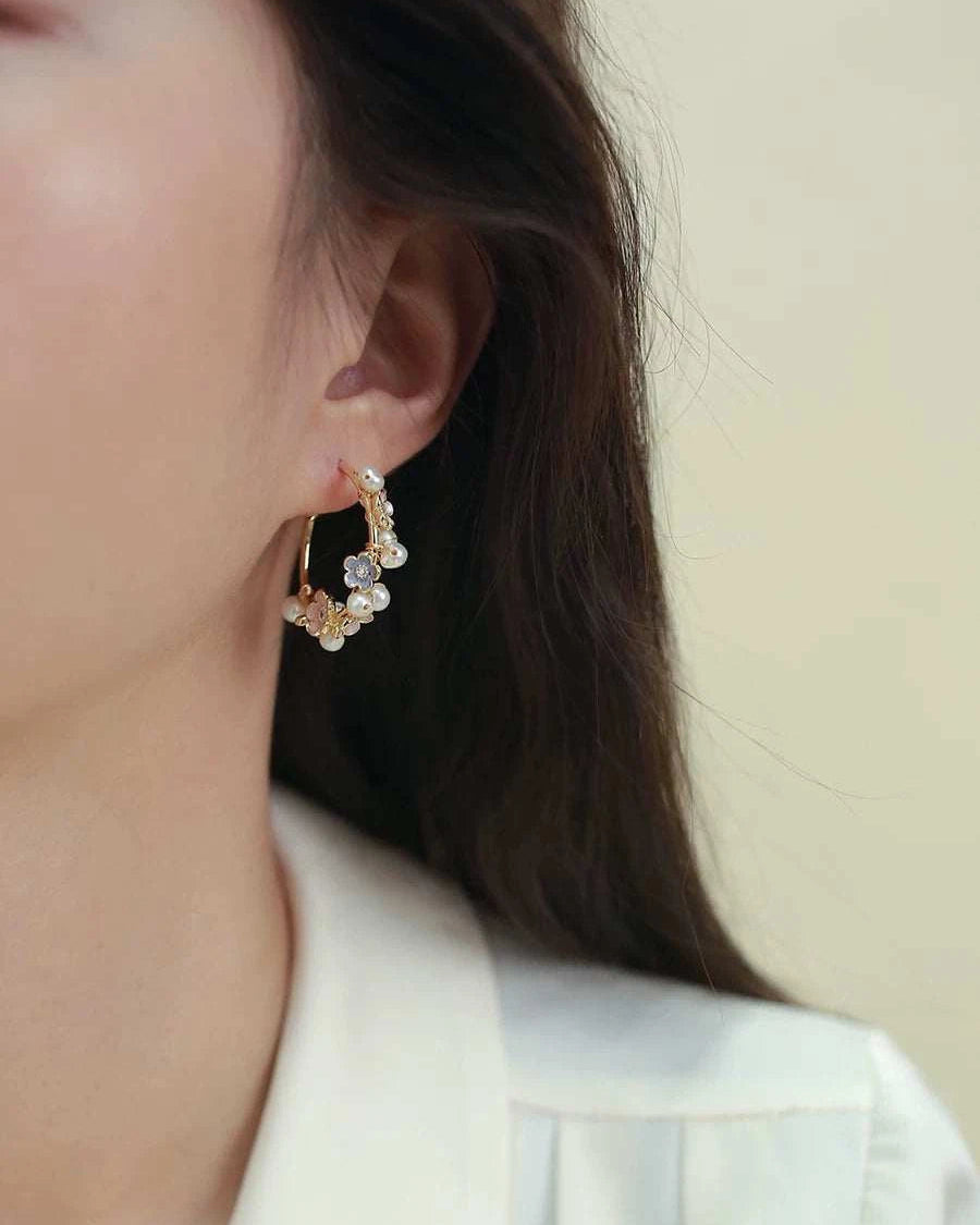 Close-up of a person wearing gold hoop earrings with small pearls against a neutral background