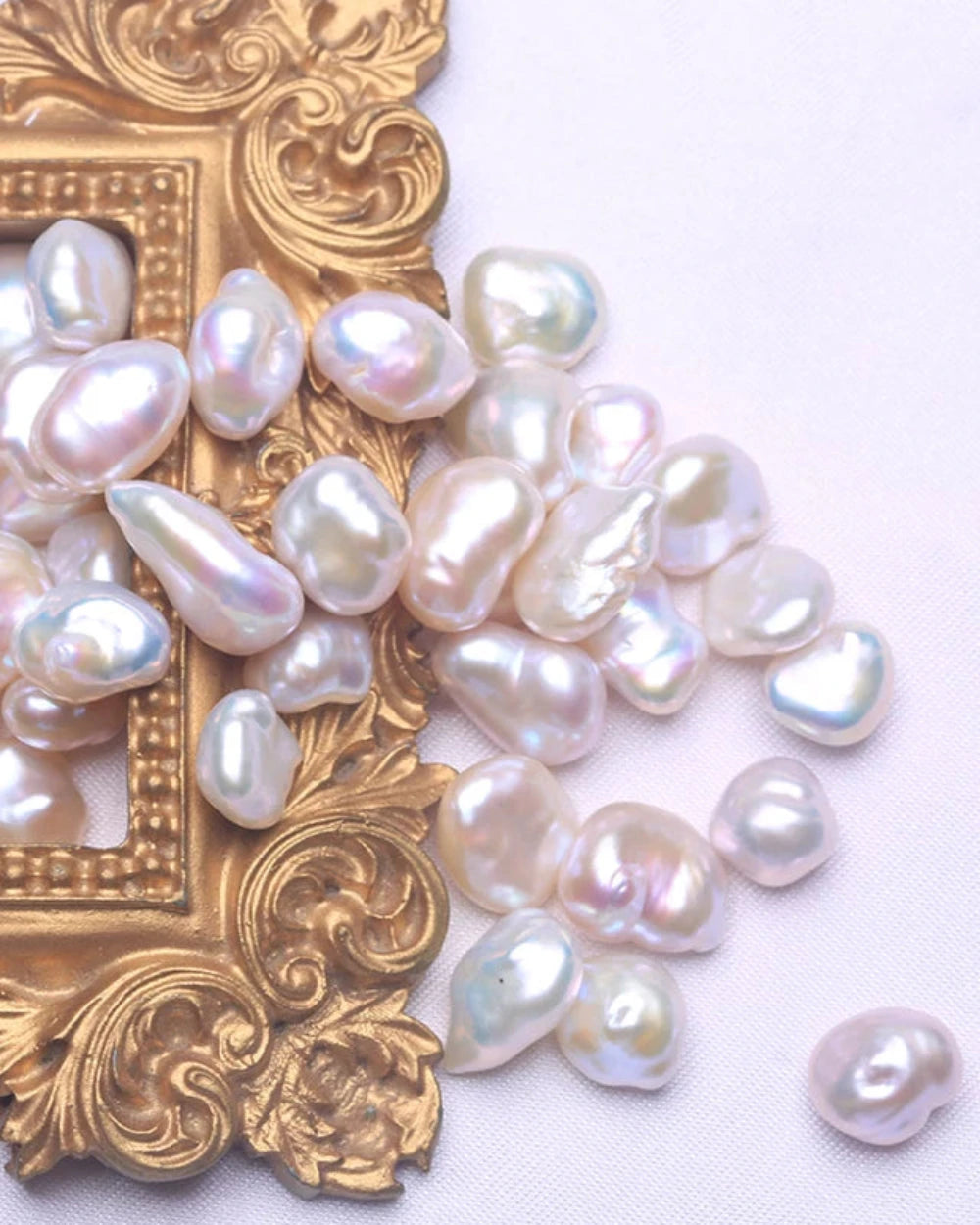 Pearls scattered on a white surface with an ornate gold frame.