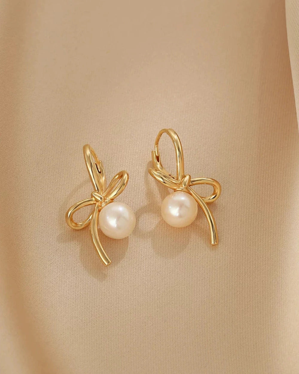 Gold earrings with pearl centers on a beige background