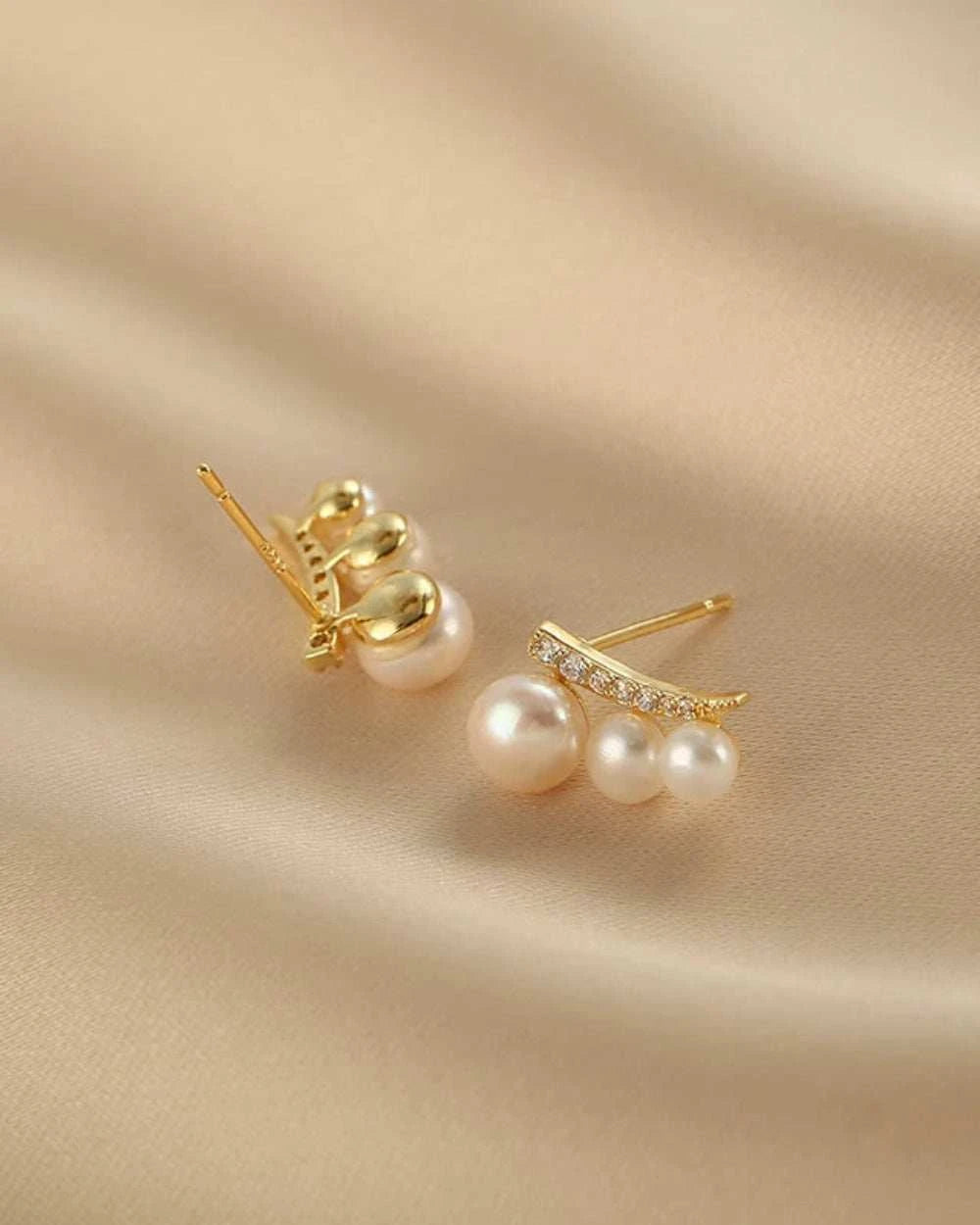 Gold and pearl earrings on a beige fabric background