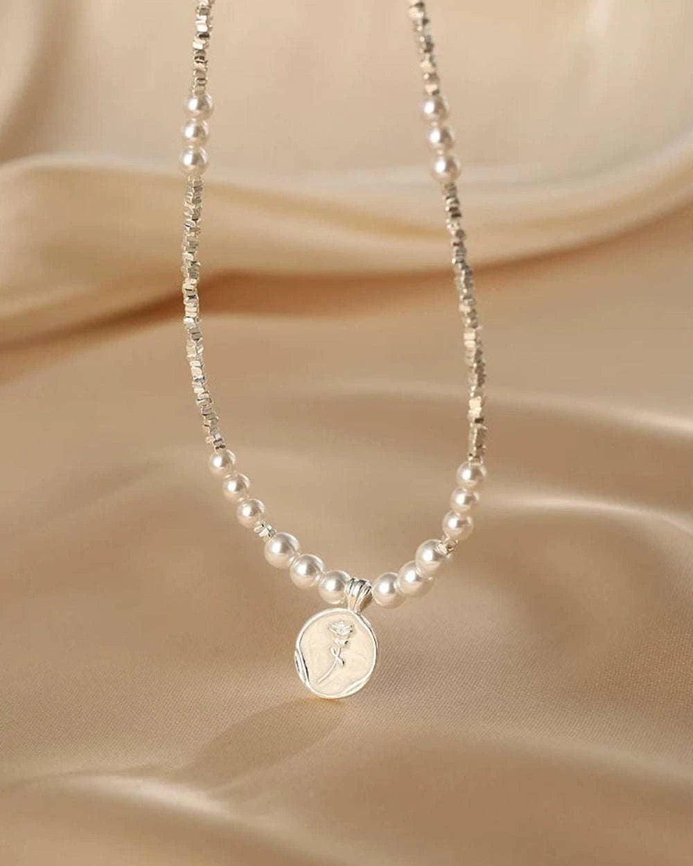 Pearl necklace with a silver pendant on a beige fabric background