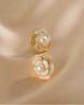 Gold and pearl flower-shaped earrings on a beige fabric background
