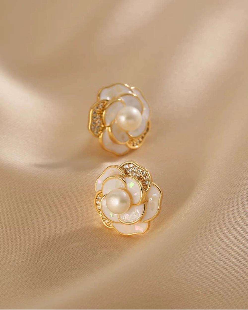 Gold and pearl flower-shaped earrings on a beige fabric background