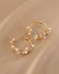 Gold hoop earrings with pearl and gemstone accents on a beige background