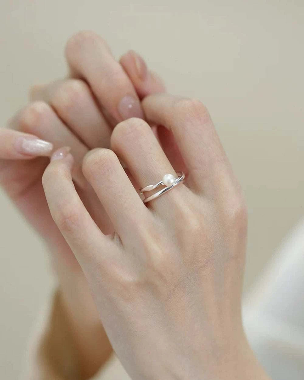 Close-up of a hand wearing a silver ring with a pearl on a neutral background