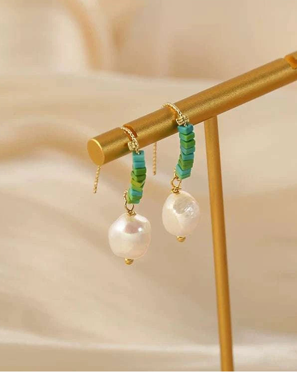 Pair of earrings with green and gold accents hanging on a gold stand against a beige background