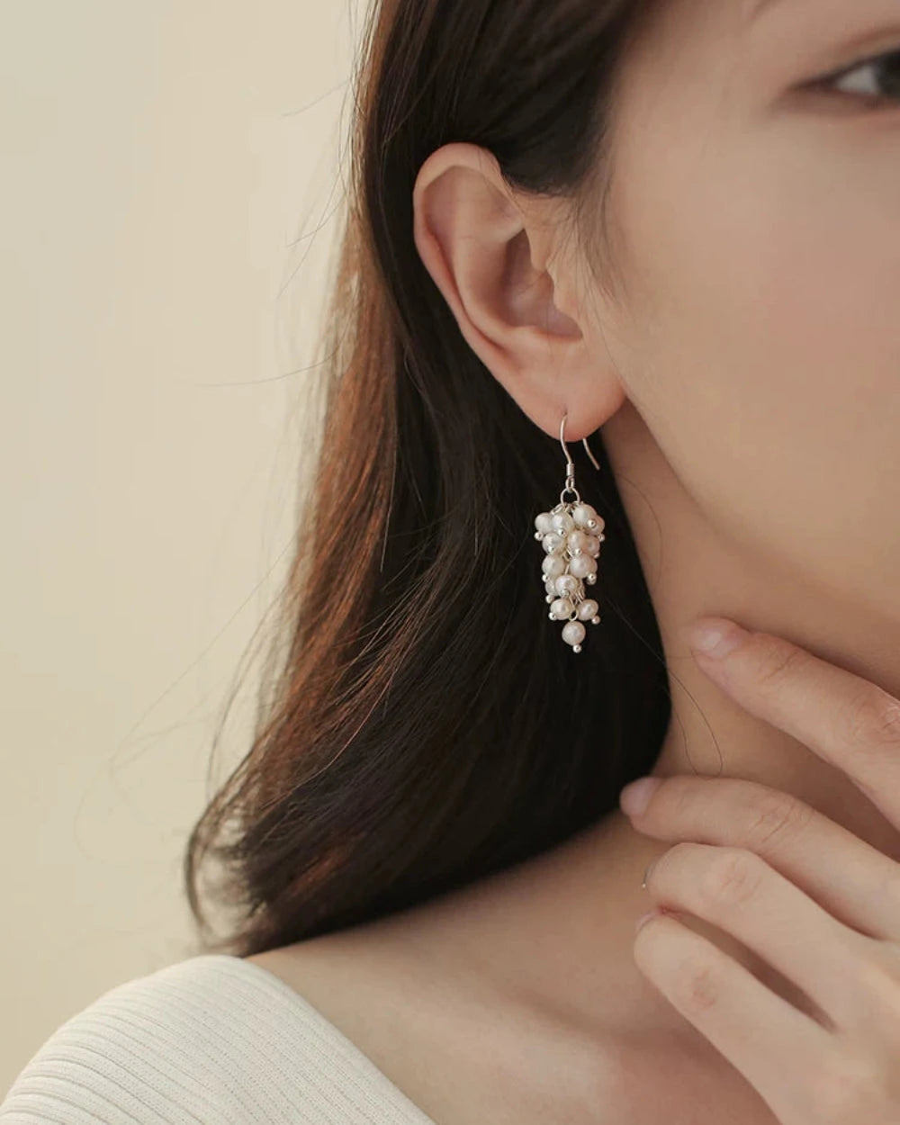 Close-up of a person wearing a delicate earring with a neutral background