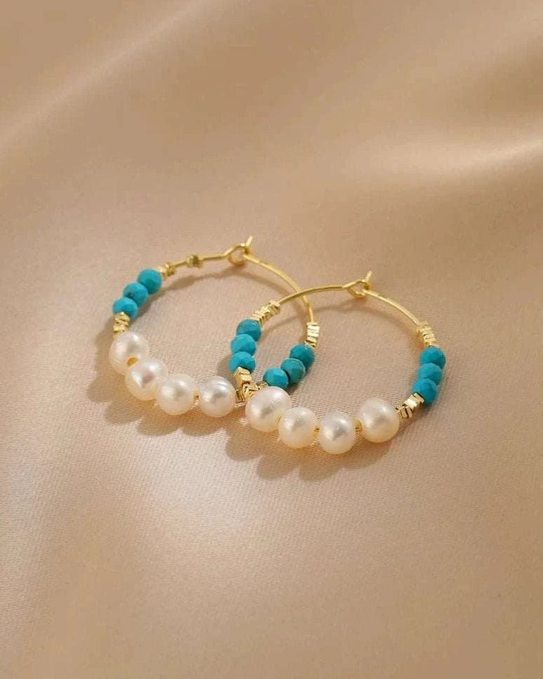 Pair of gold hoop earrings with pearl and turquoise beads on a beige background