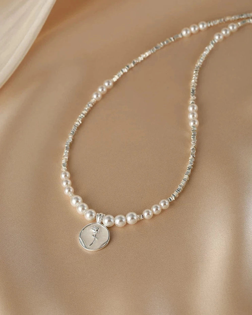 Pearl necklace with a silver pendant on a neutral background