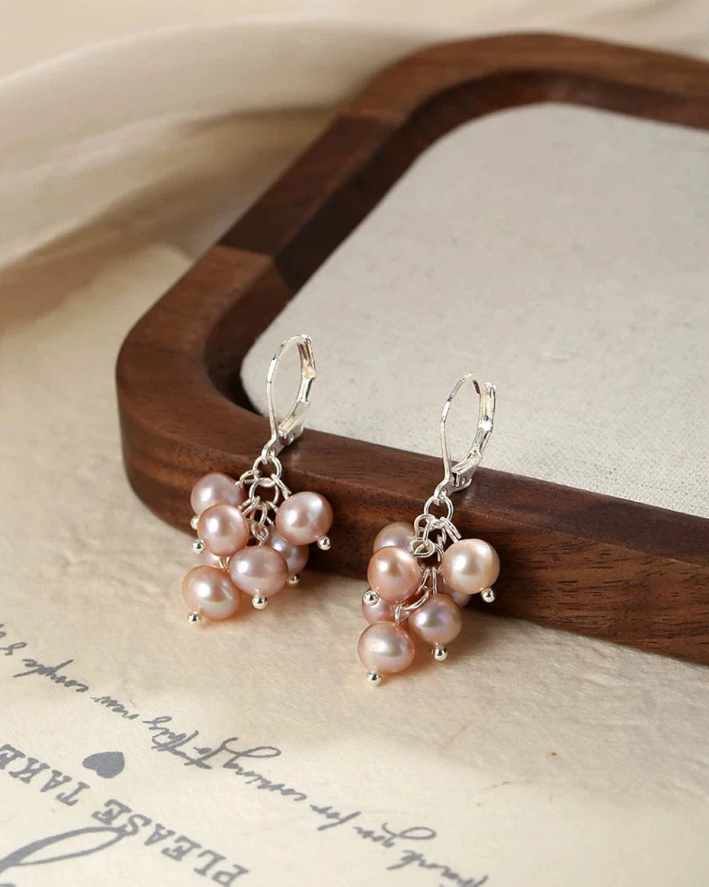 Pair of pearl earrings on a wooden stand with a beige background