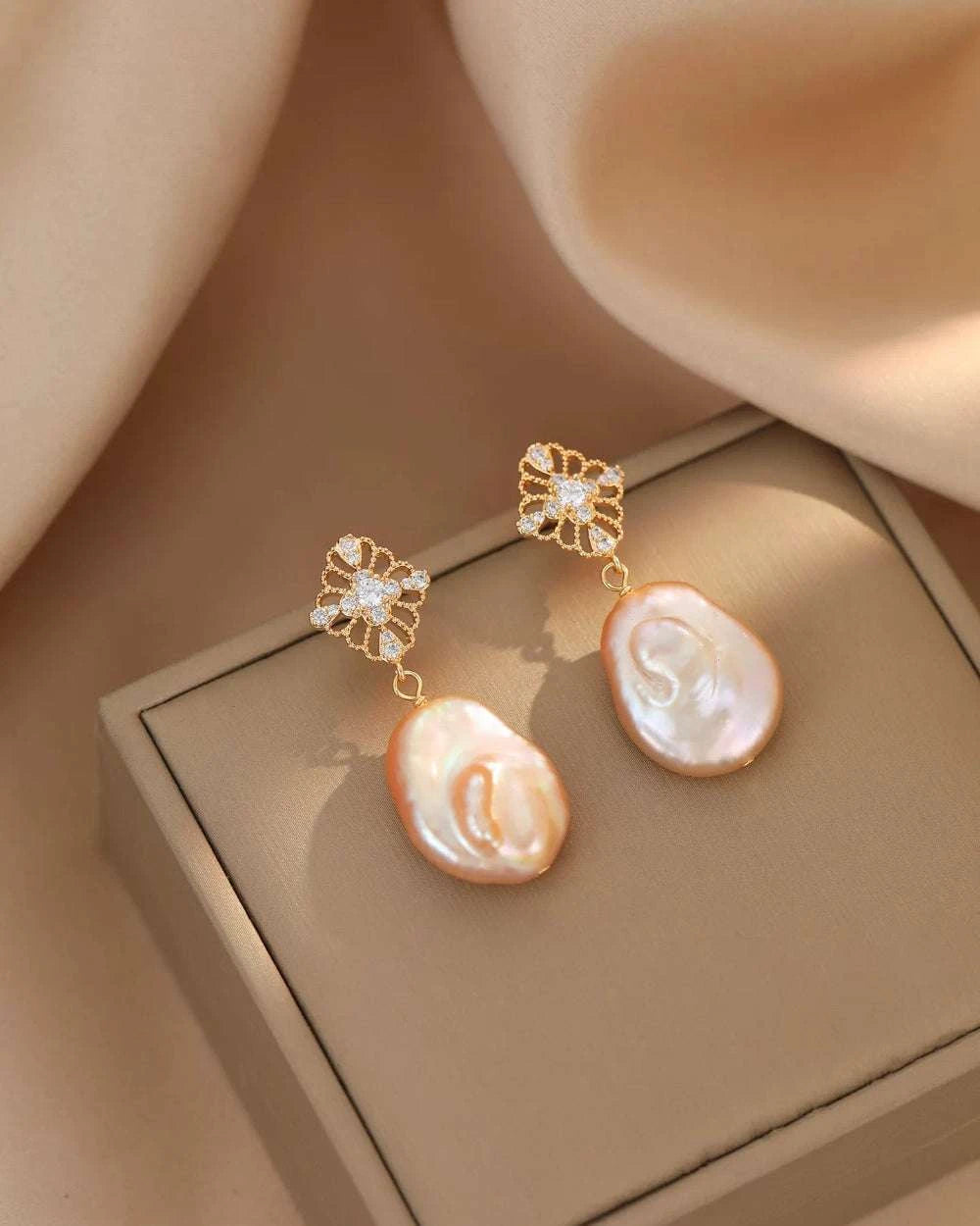 Pearl earrings with gold floral clasps on a beige surface