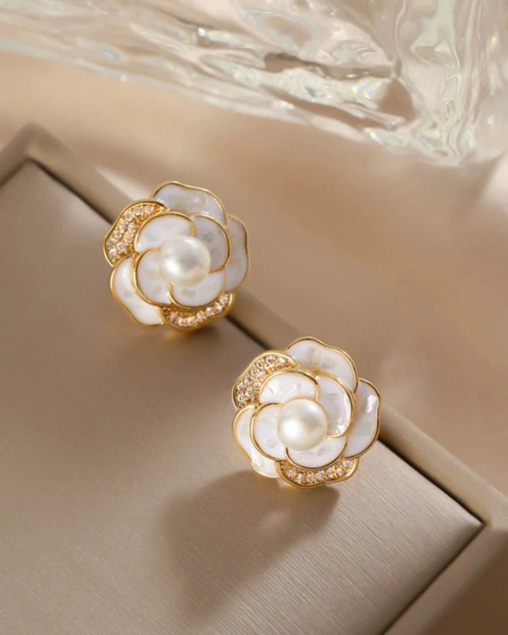 Pair of floral earrings with gold and pearl design on a beige surface.