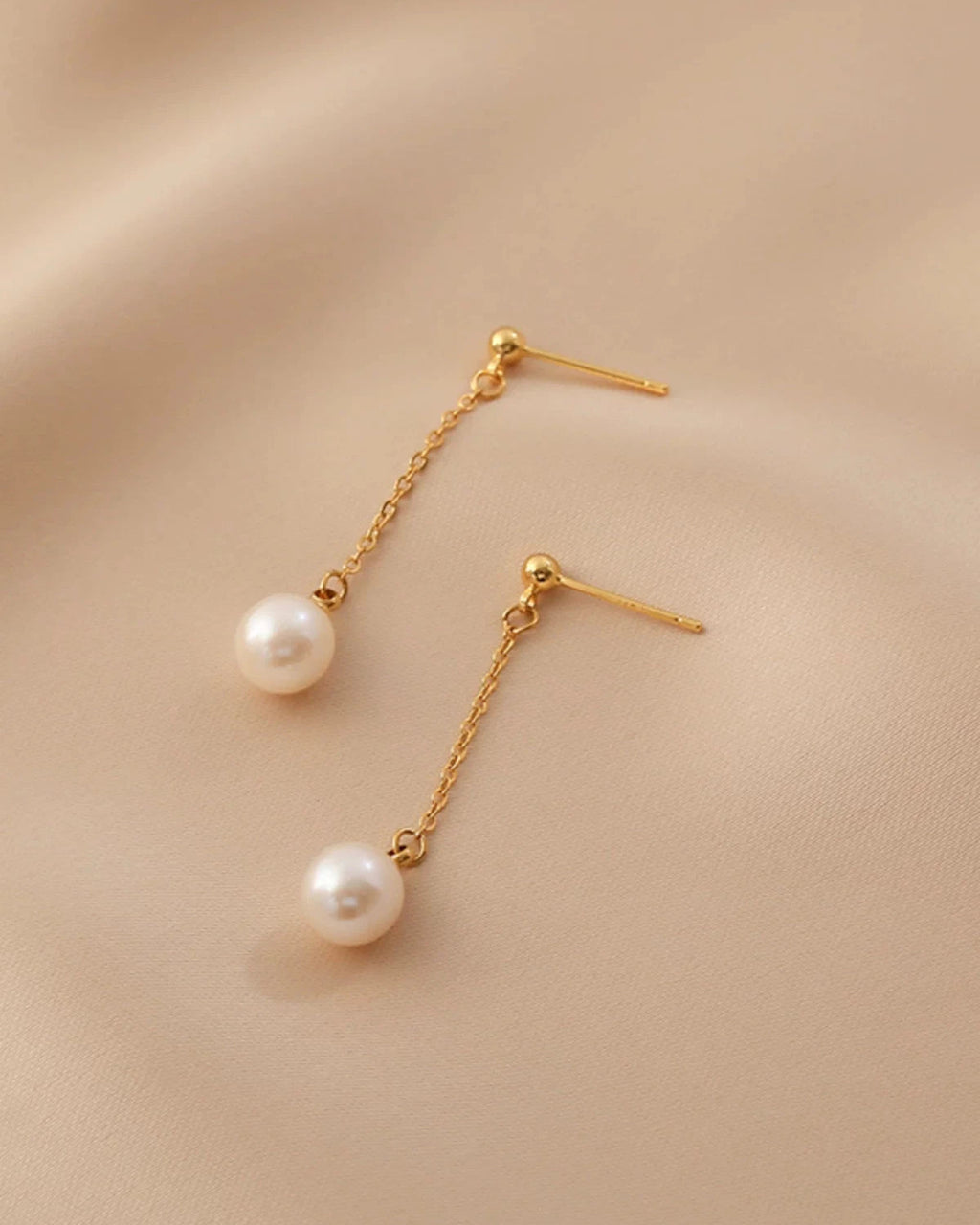 Gold earrings with pearl drops on a beige background