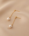 Gold earrings with pearl drops on a beige background