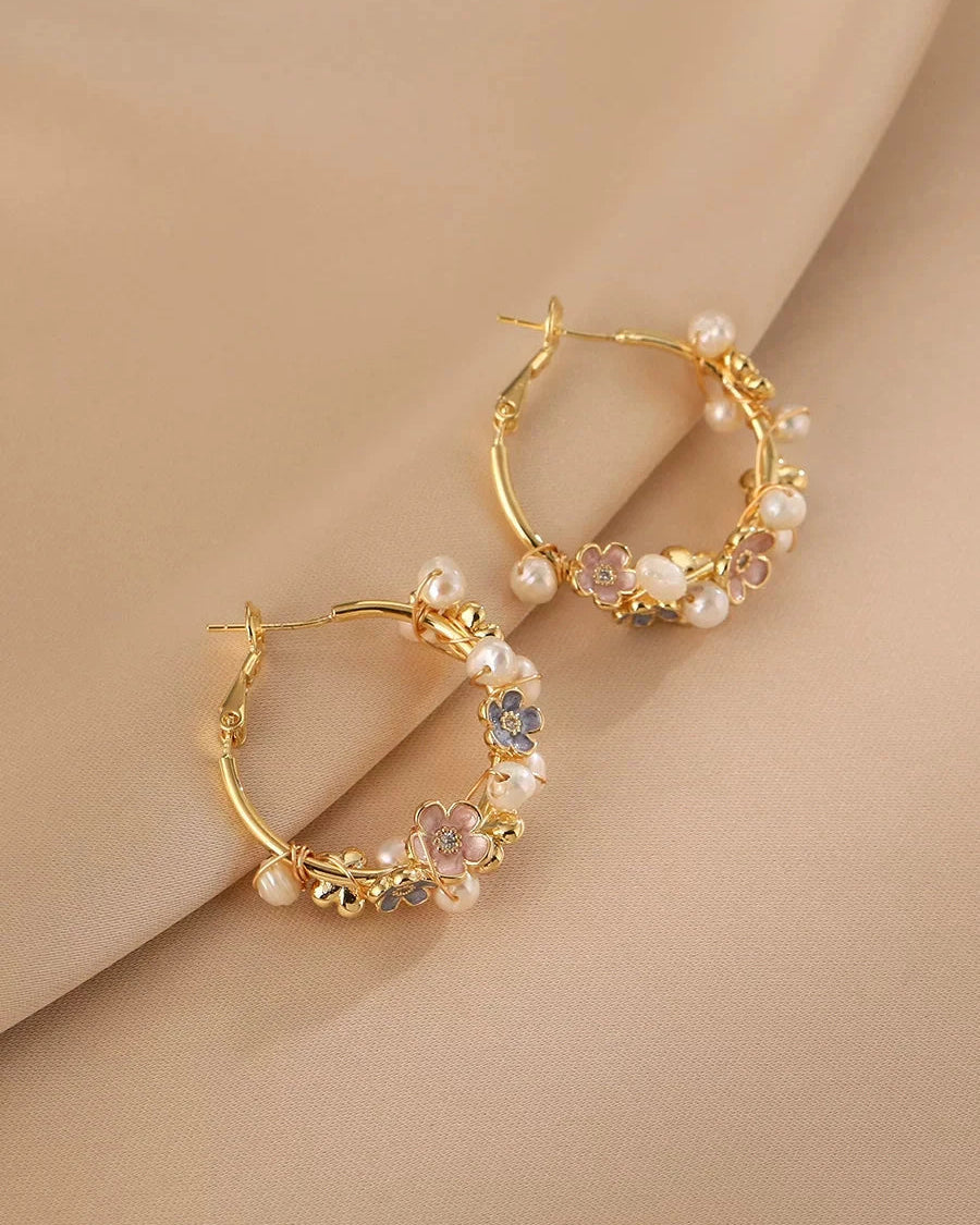 Gold hoop earrings with floral and pearl details on a beige background