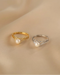 Two pearl rings, one gold and one silver, on a beige fabric background