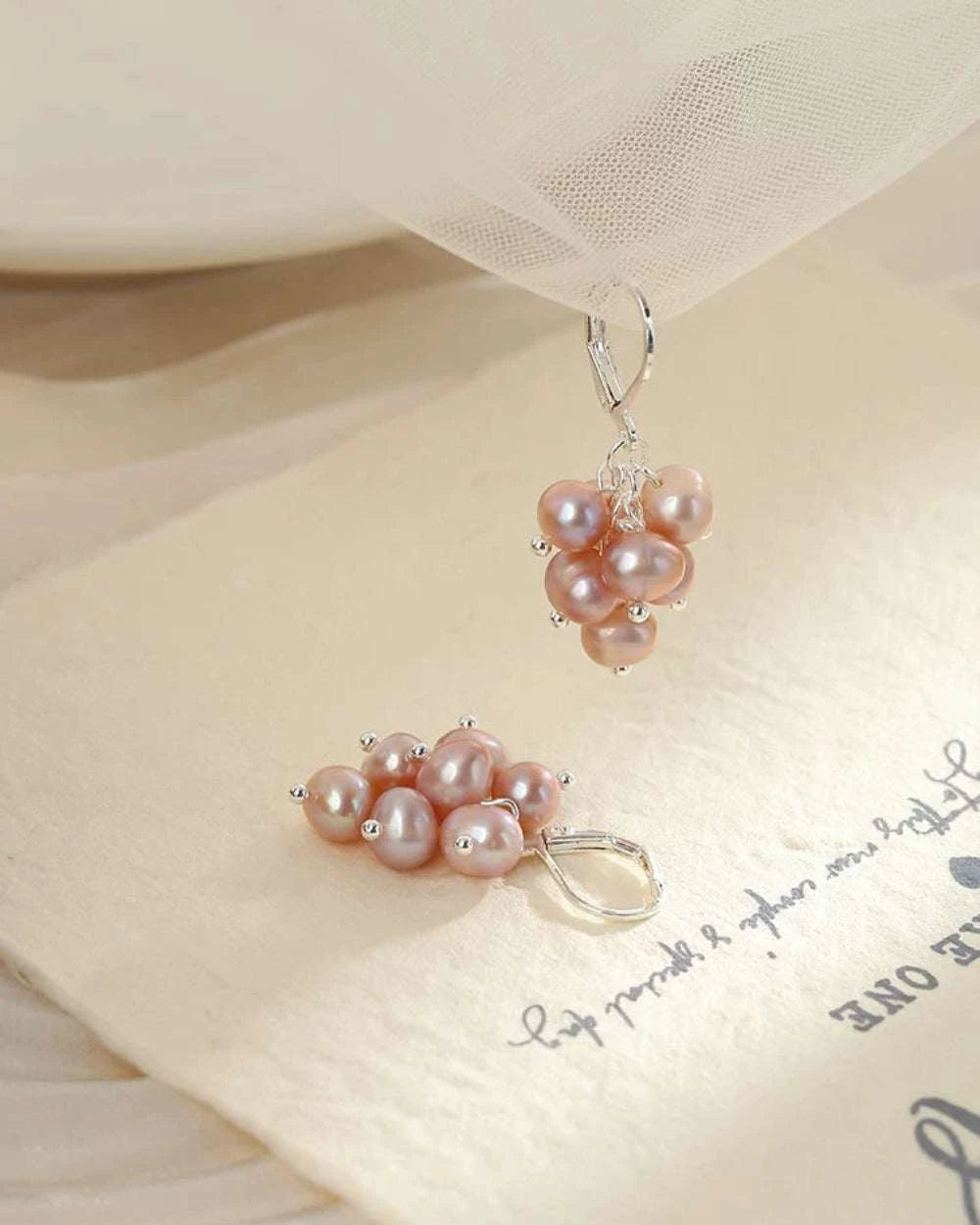 Pair of pink pearl earrings on a textured fabric background