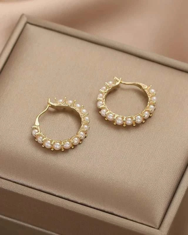 Gold hoop earrings with pearls on a beige jewelry box