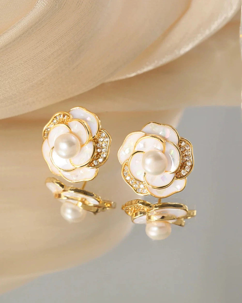 Gold and pearl flower-shaped earrings on a soft beige background