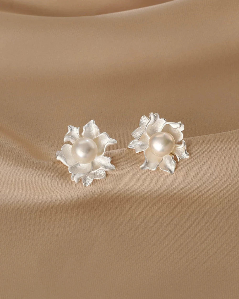 Pair of silver earrings with pearl centers on a beige fabric background