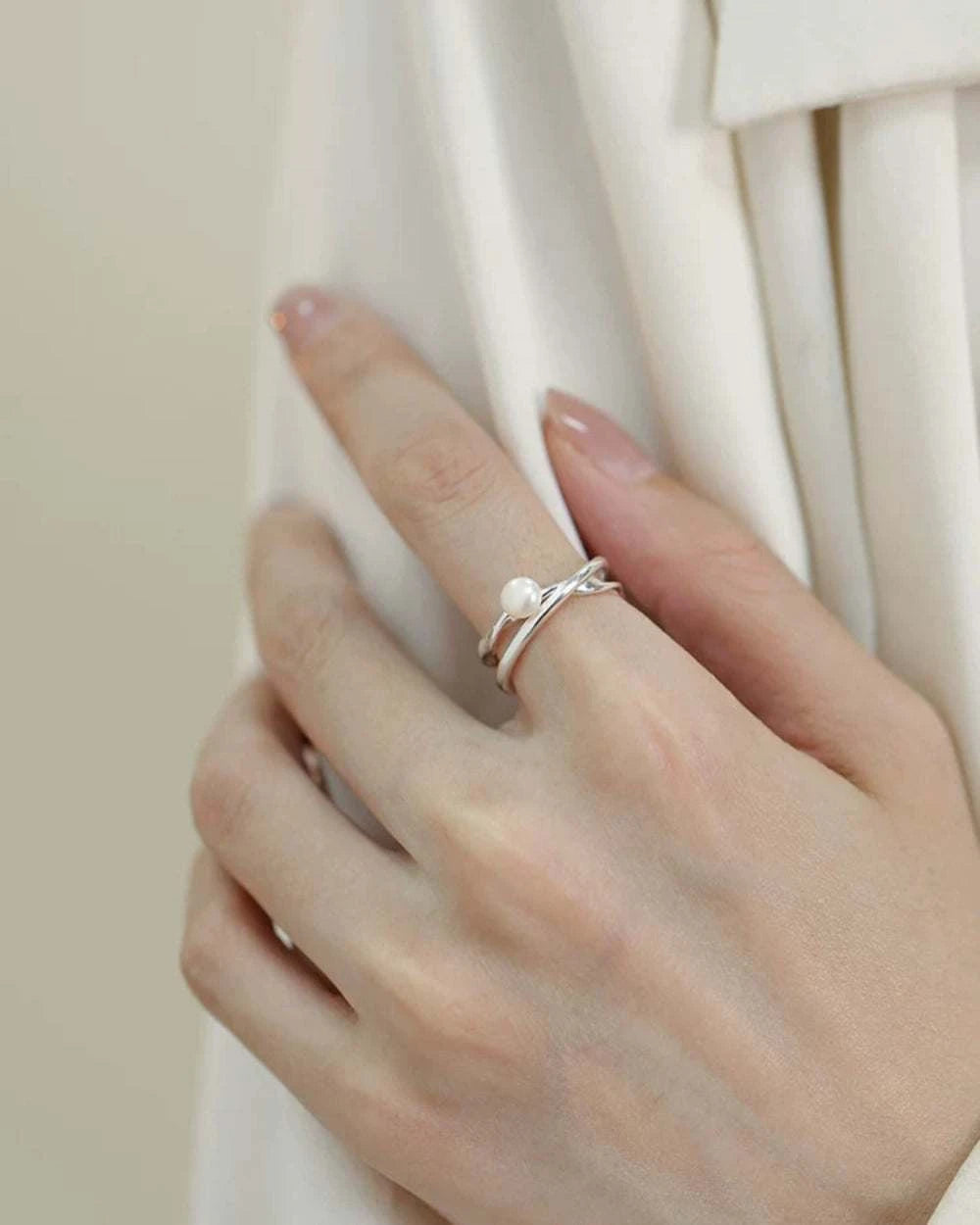 Hand wearing a silver ring with a pearl on a white background