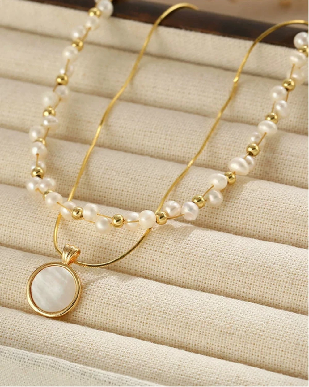 Pearl and gold necklace on a textured beige surface