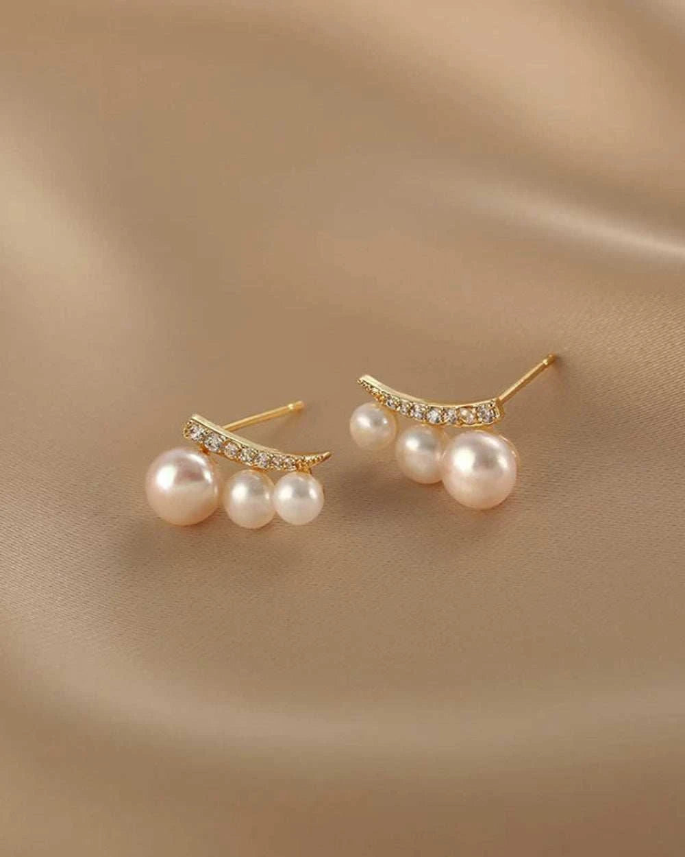 Pair of pearl earrings with gold accents on a beige fabric background
