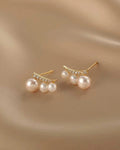 Pair of pearl earrings with gold accents on a beige fabric background
