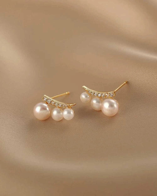 Pair of pearl earrings with gold accents on a beige fabric background