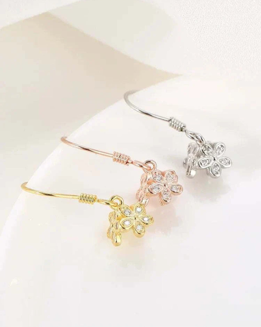 Three floral-shaped bracelets in gold, rose gold, and silver on a white surface.