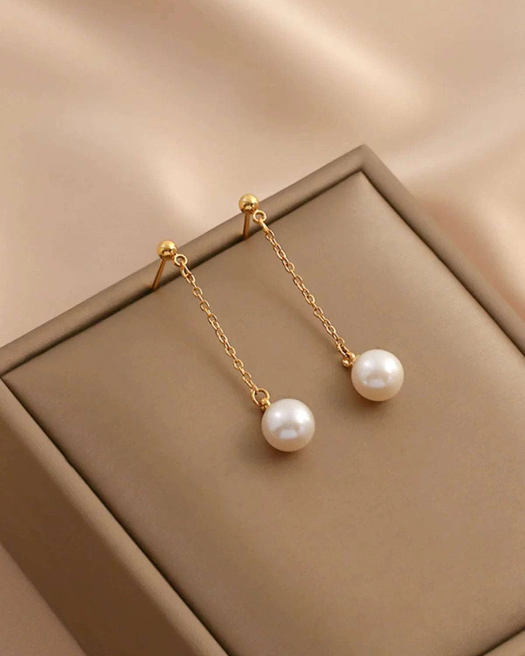 Pearl earrings with gold chains on a beige surface