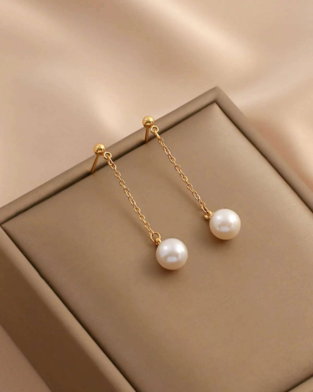 Pearl earrings with gold chains on a beige surface