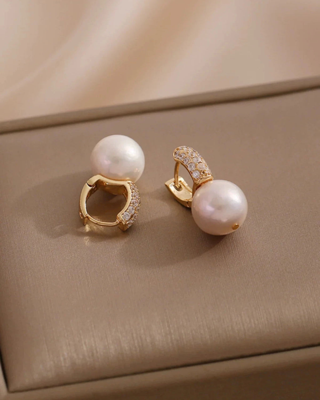 Pair of pearl earrings with gold accents on a beige surface