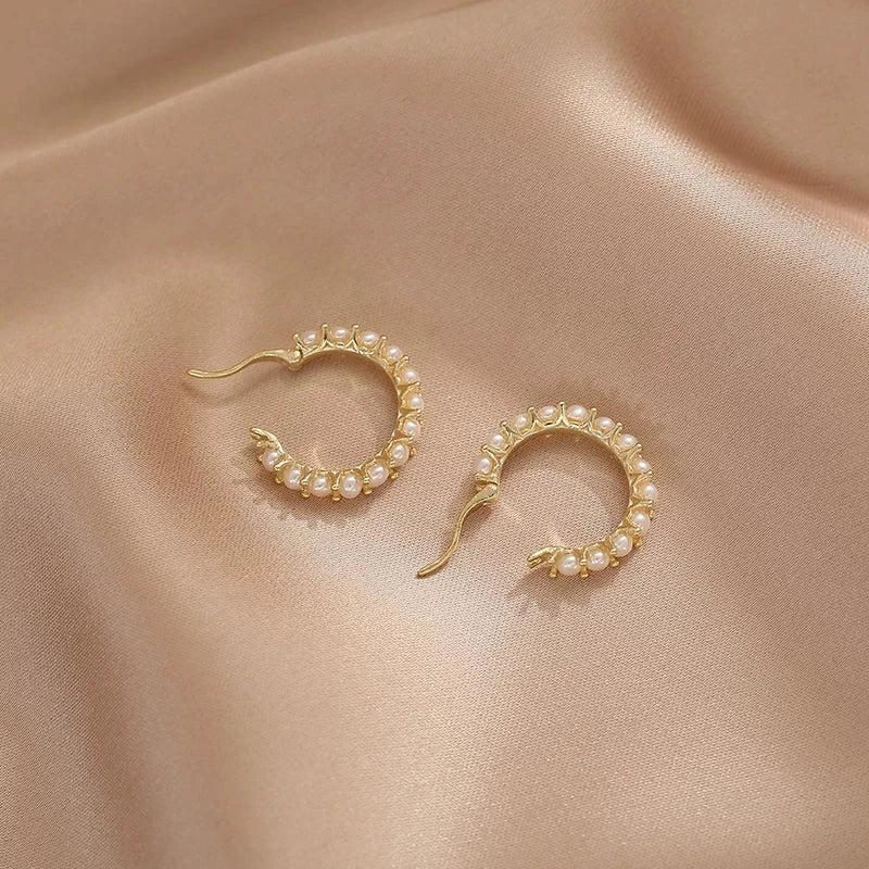 Gold hoop earrings with pearls on a beige fabric background