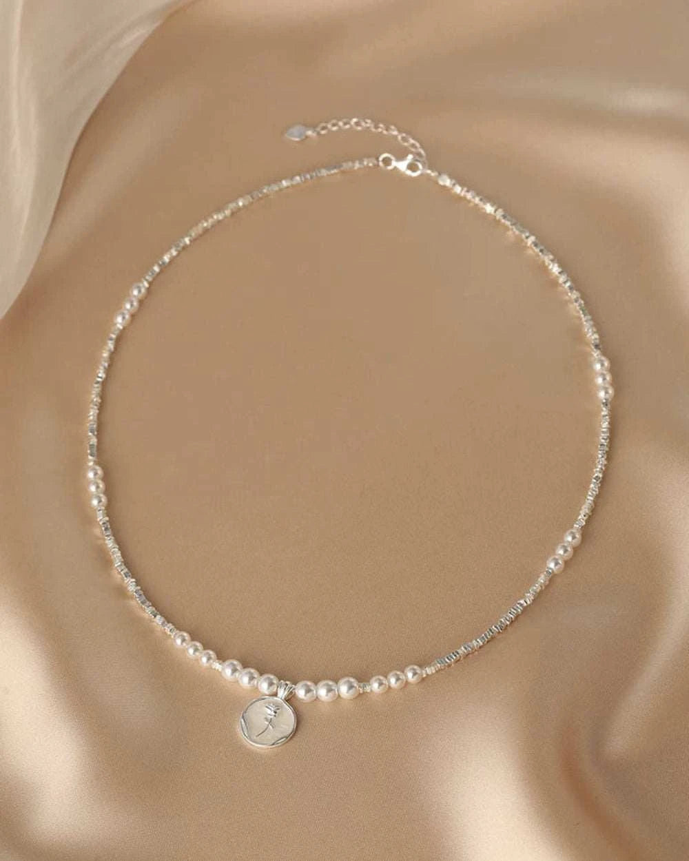 Pearl necklace with a silver pendant on a beige fabric background