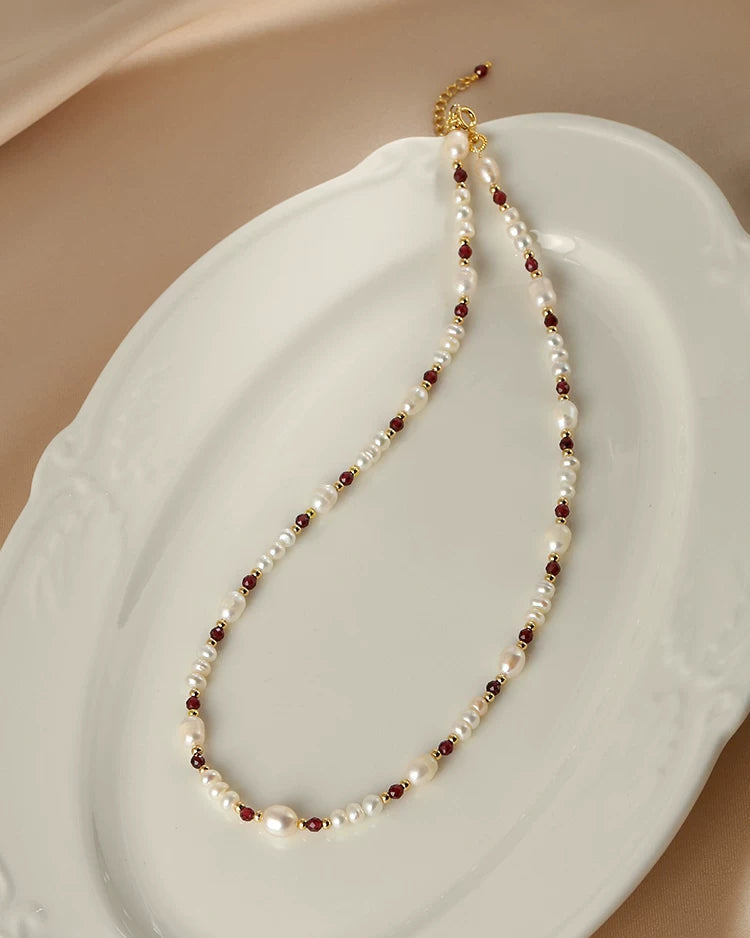 Pearl and red bead necklace on a white shell with a beige background