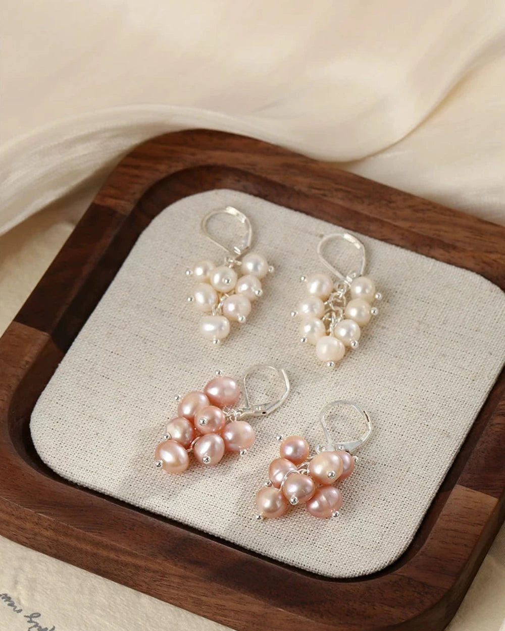 Pair of pearl earrings on a wooden tray with a beige fabric background