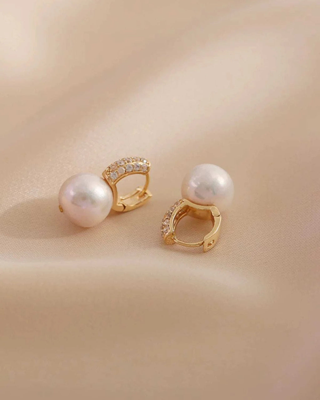 Pair of pearl earrings with gold accents on a beige background