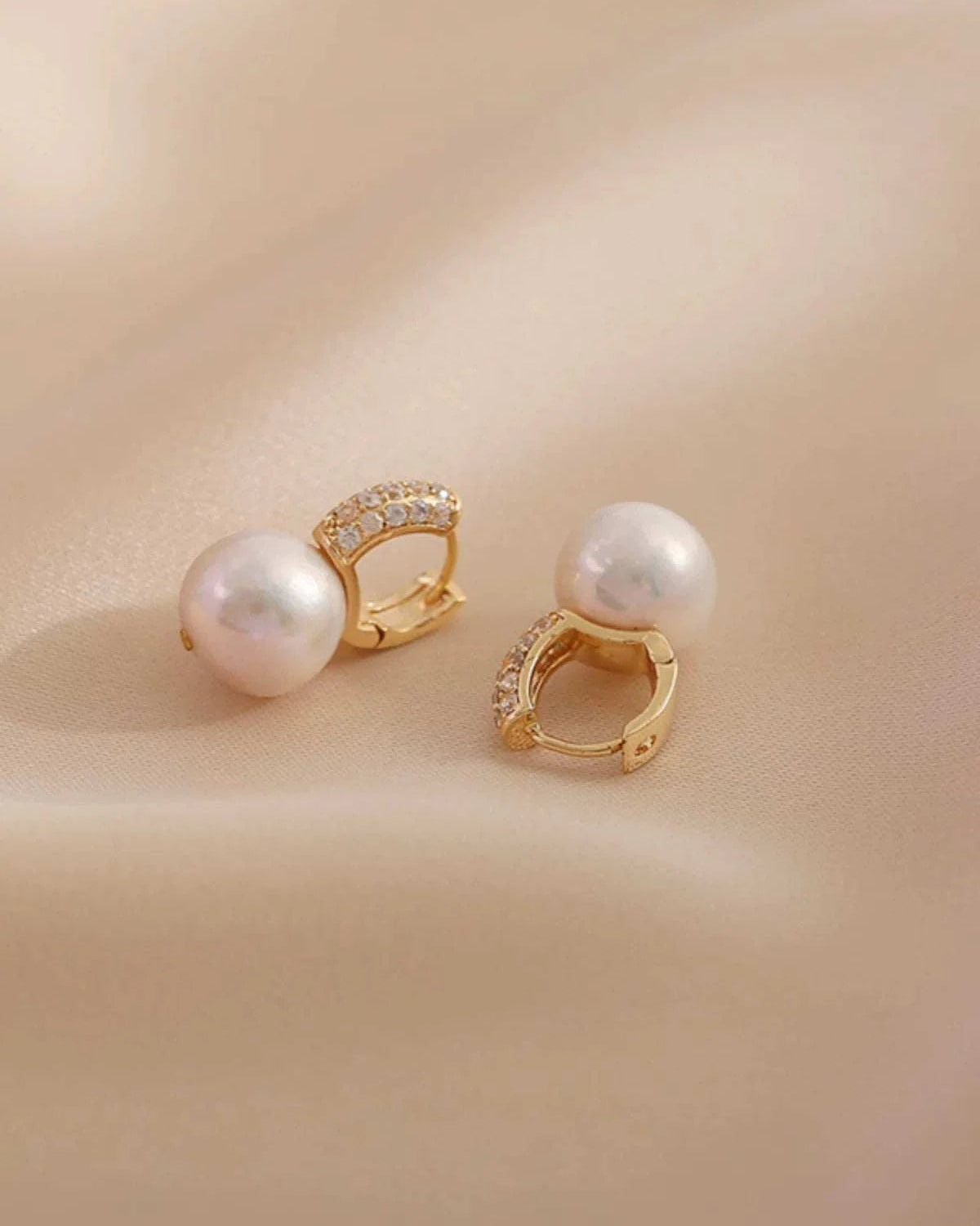 Pair of pearl earrings with gold accents on a beige background